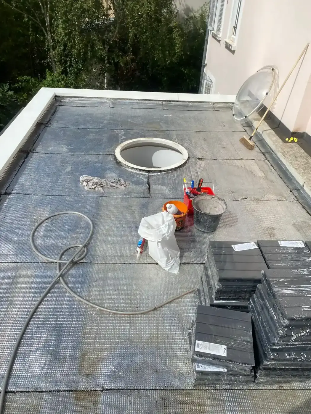 Début de chantier à Colombes : ancienne étanchéité argentée déposée, puits de lumière ouvert et dalles composite stockées sur la terrasse