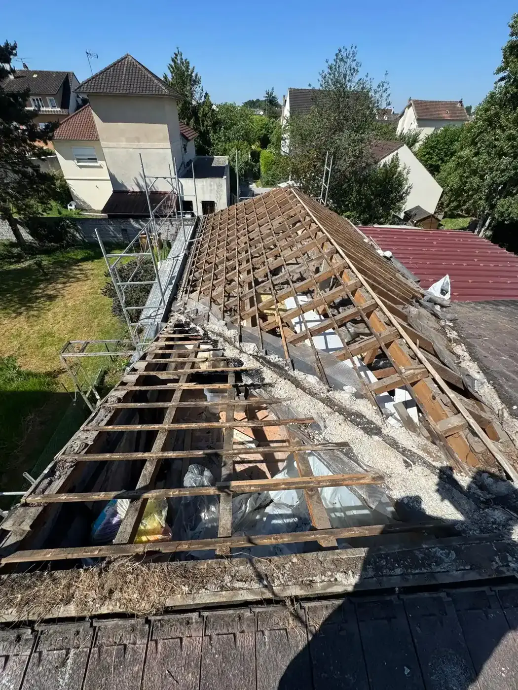 Dépose de la couverture à Noisy-le-Grand : charpente à nu et débris le long de l'arêtier, échafaudage en place